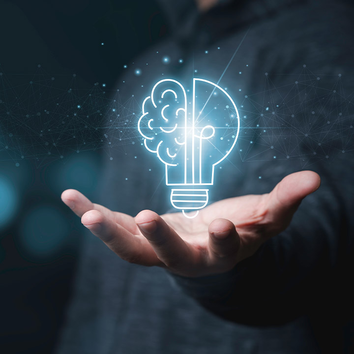 Above an outstretched hand with its fingertips pointing towards the viewer, a blue light bulb floats, half of which symbolises a brain.