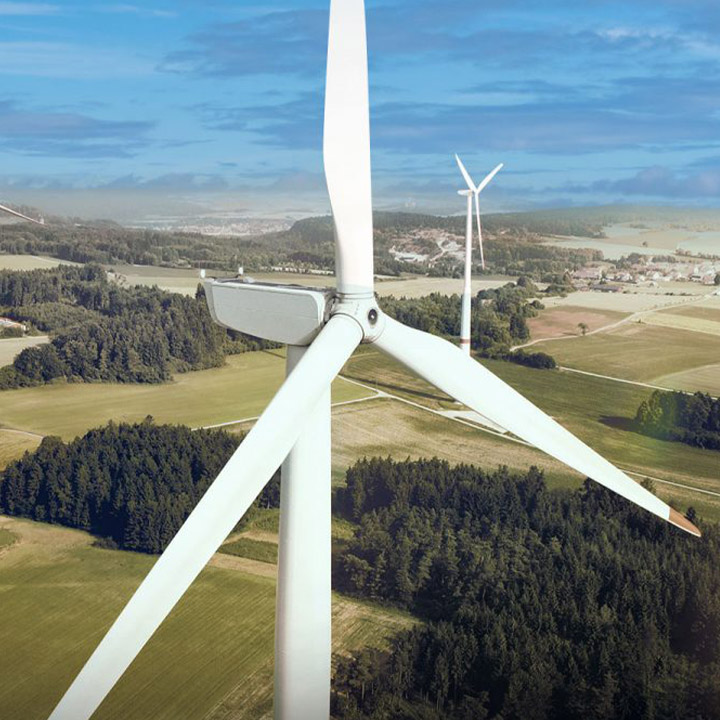 Frontal view of the blades of a white wind turbine from a bird's eye perspective with a hilly background.