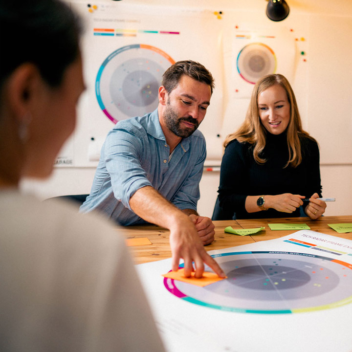 A BMW employee is placing an orange Post-it note on a circular graphic that has been printed out and is lying on a table.