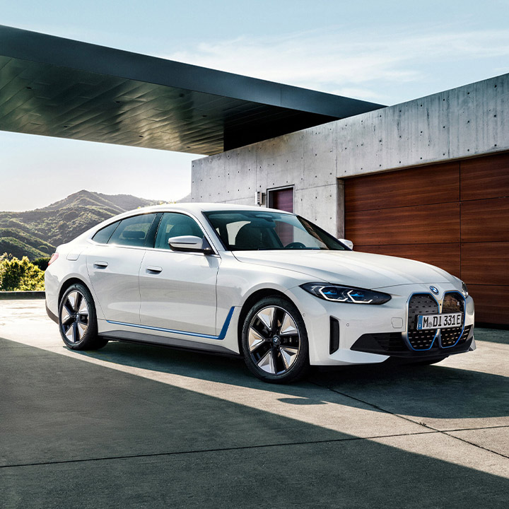 A white BMW saloon car is parked in front of a modern bungalow. In the background, we can see rolling hills.