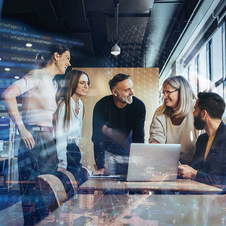 A group of four BMW employees are all laughing as they look at a laptop lying between them on the conference table.