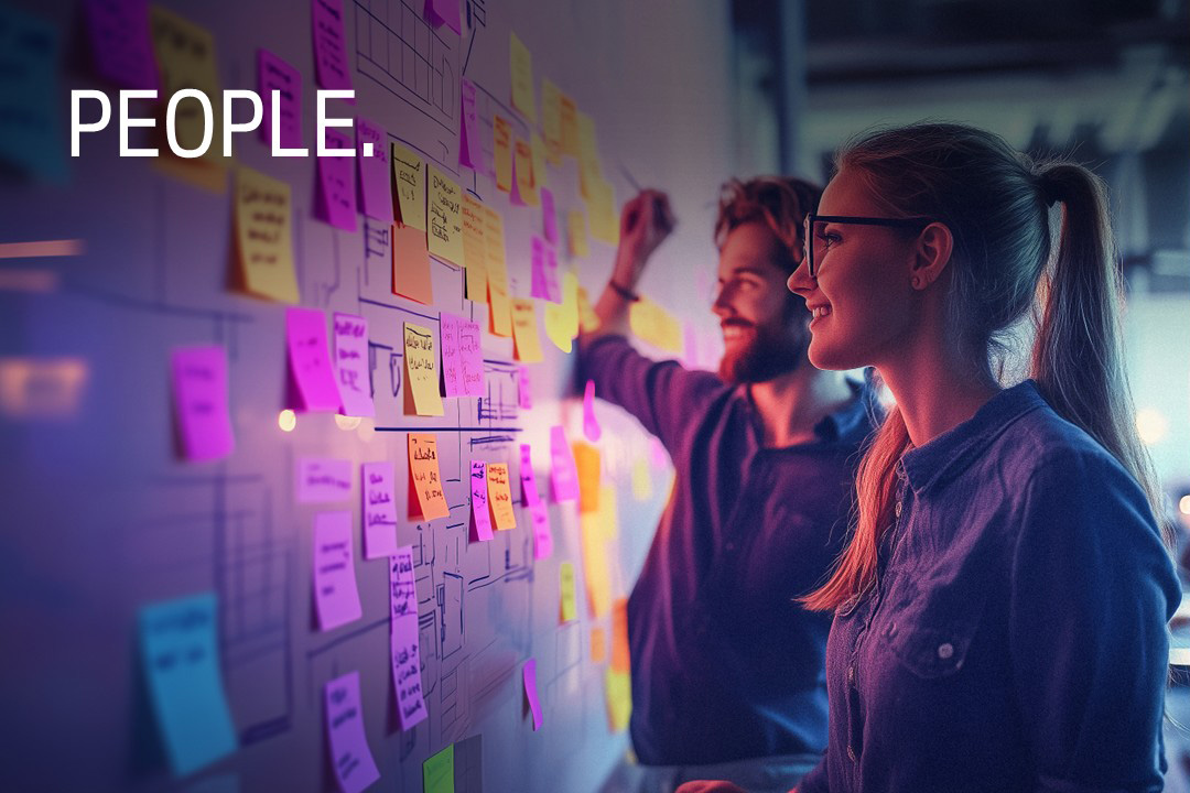 Two people planning at a whiteboard covered with colorful sticky notes.