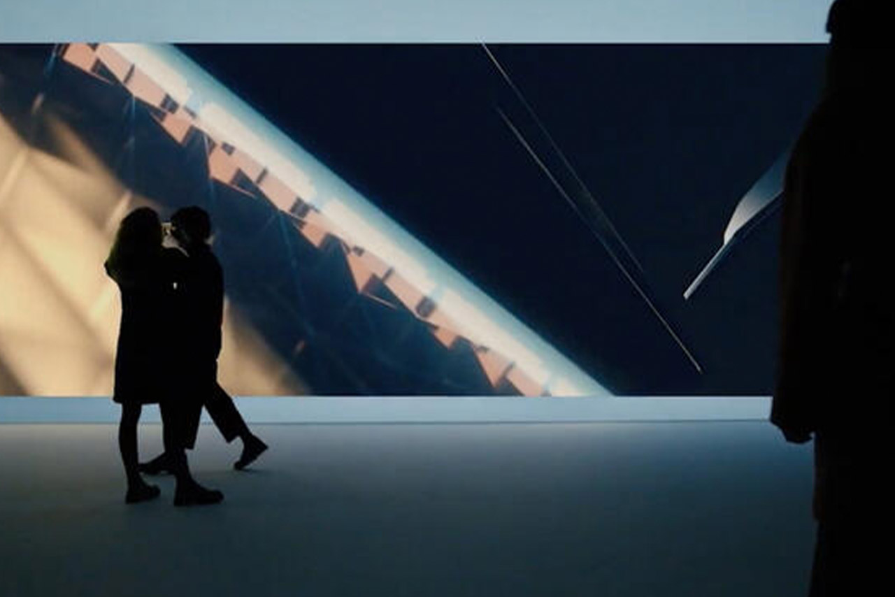 Two people stand as silhouettes in front of an iconically designed graphic background, as large as a cinema screen.